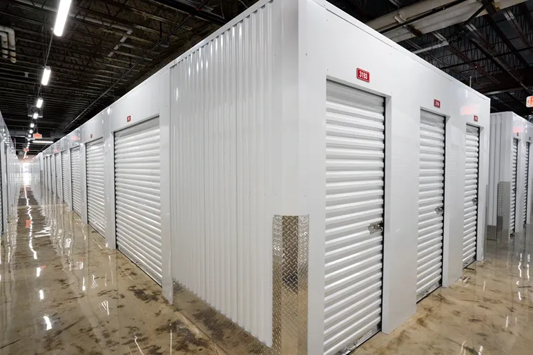 Climate-controlled storage hallway with red roll-up doors and natural light from windows
