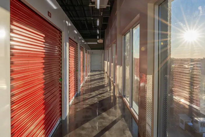 Climate-controlled storage hallway with red roll-up doors and natural light from windows