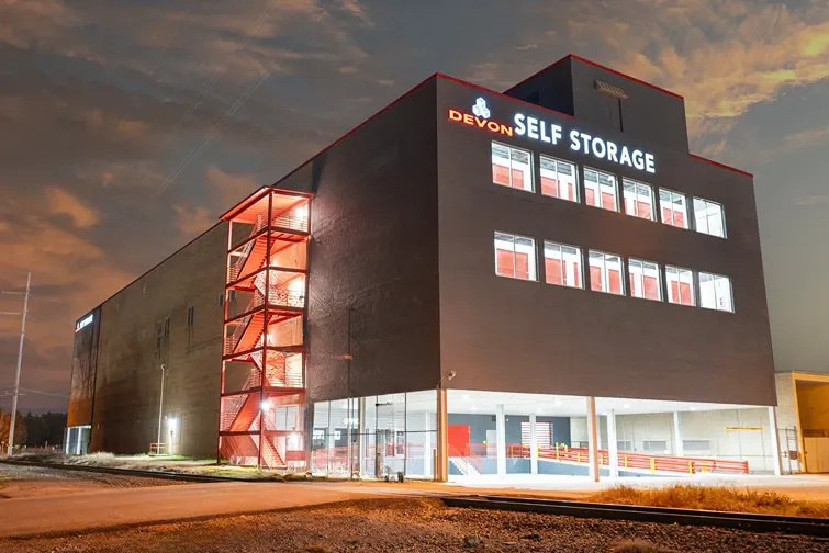 Devon Self Storage multi-story facility exterior at dusk with illuminated signage and covered drive-through access