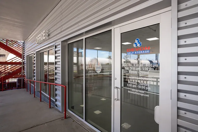 Devon Self Storage office entrance with glass doors displaying hours and contact information