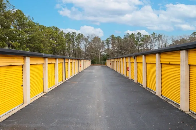 Wide drive aisle between rows of outdoor storage units with yellow roll-up doors